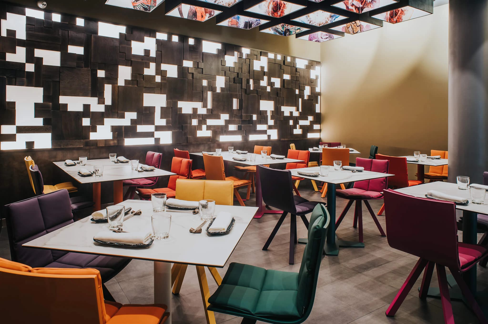 Colourful dining chairs beneath a patterned screen in Jaxana restaurant