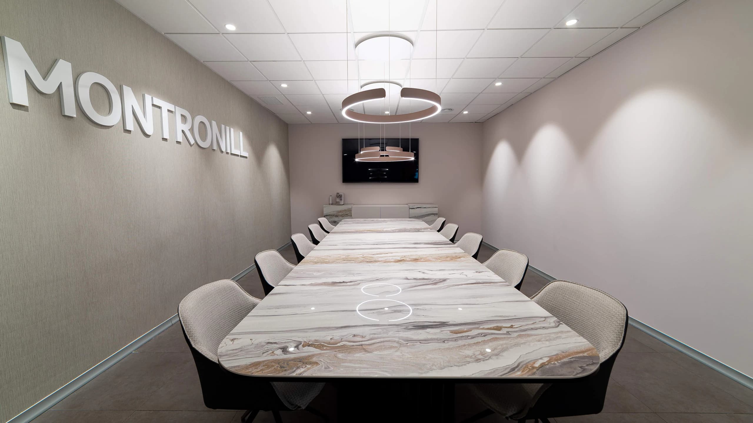 A long marble-effect meeting table with upholstered chairs in a company boardroom