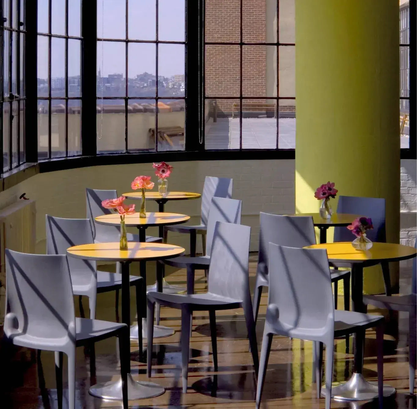 Grey Bellini chairs and yellow café tables beside tall factory windows