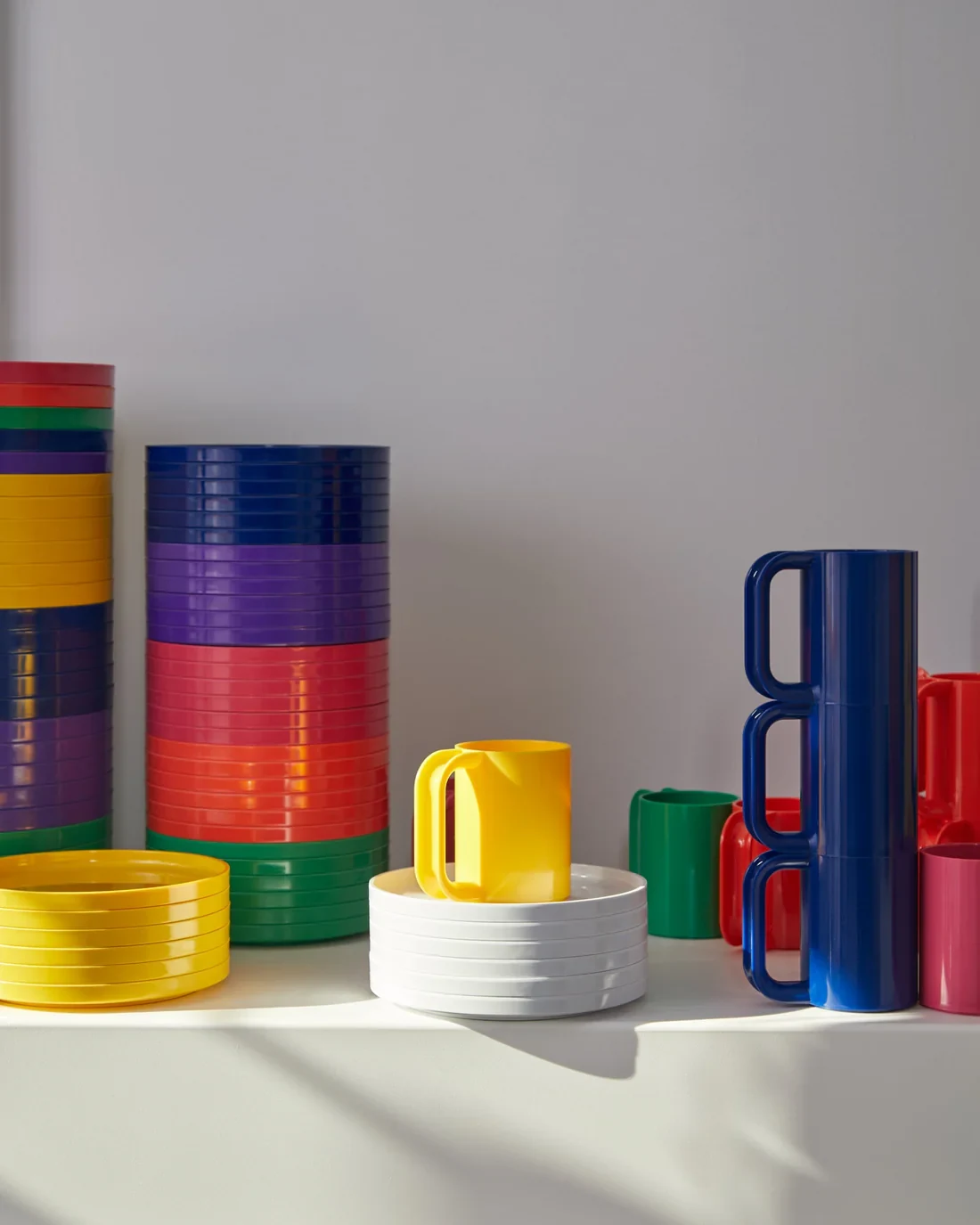 Stacks of Hellerware plates, bowls and mugs in bright colours on a white shelf