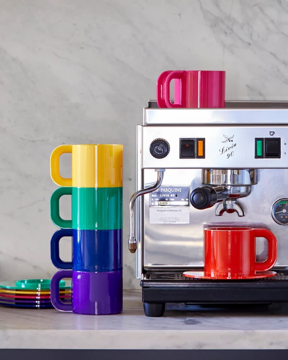Colourful Hellerware cups and saucers stacked beside an espresso machine