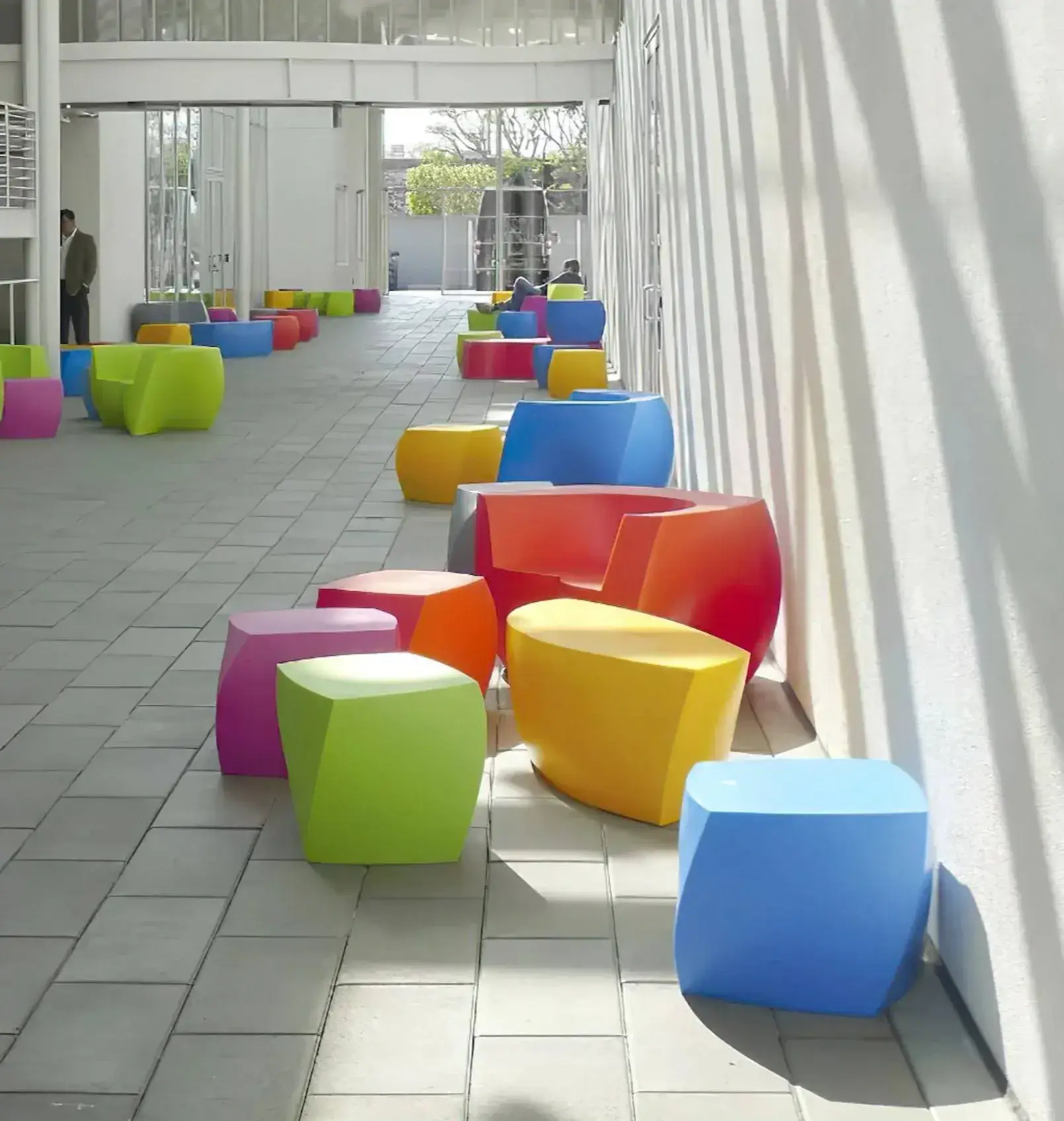 Bright red, blue, green and yellow Gehry chairs in a sunlit studio with tall windows at Gehry Partners