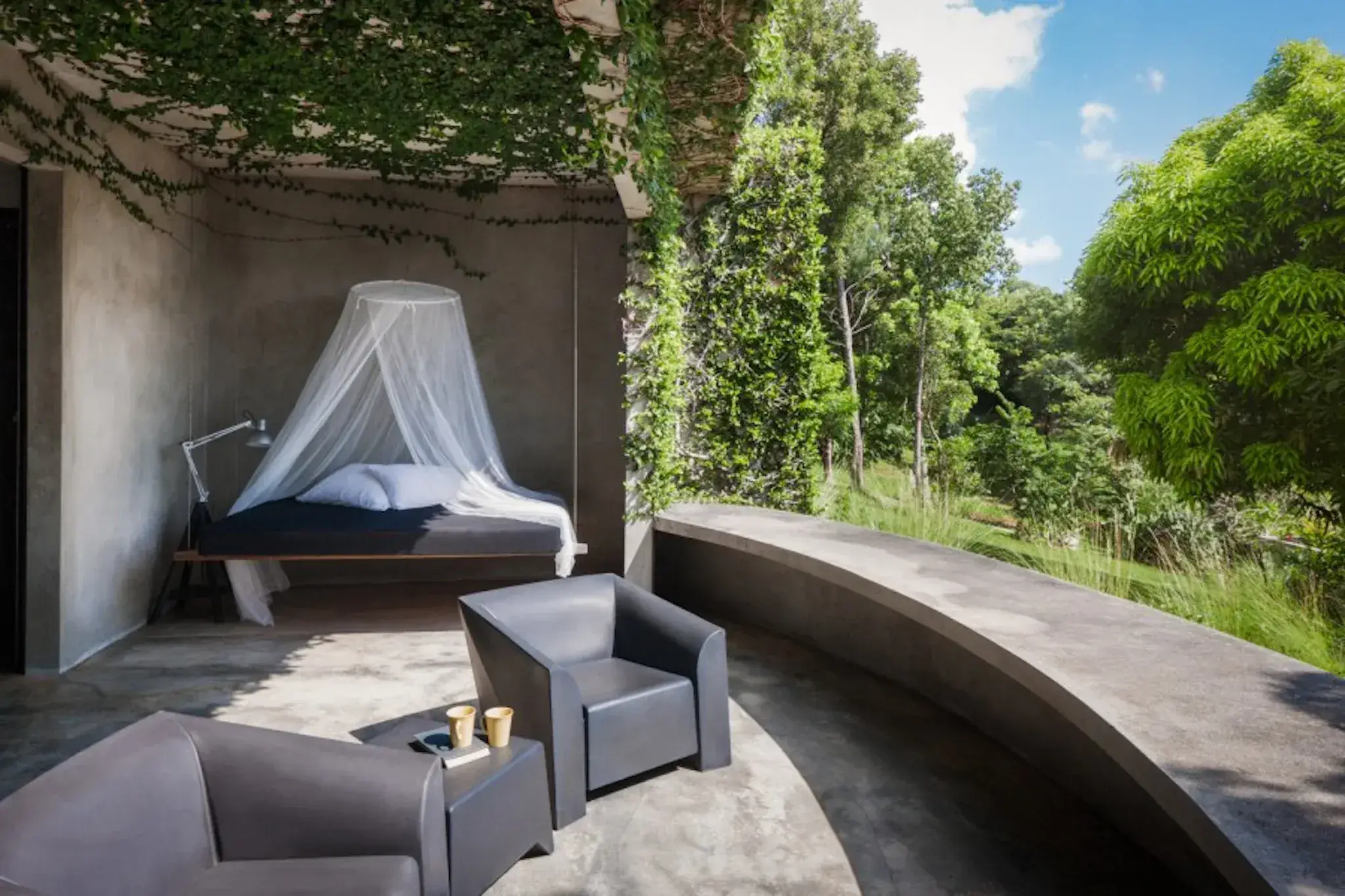 Grey Heller armchairs on a concrete terrace beside an open-air bedroom at Hix Island House
