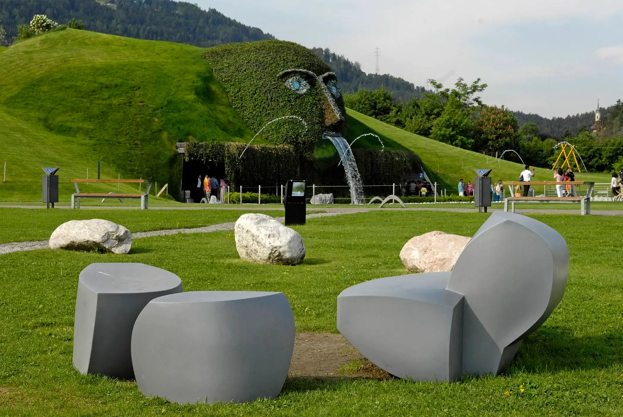 Grey Heller lounge seating on a lawn among boulders below green hills at Swarovski Kristallwelten