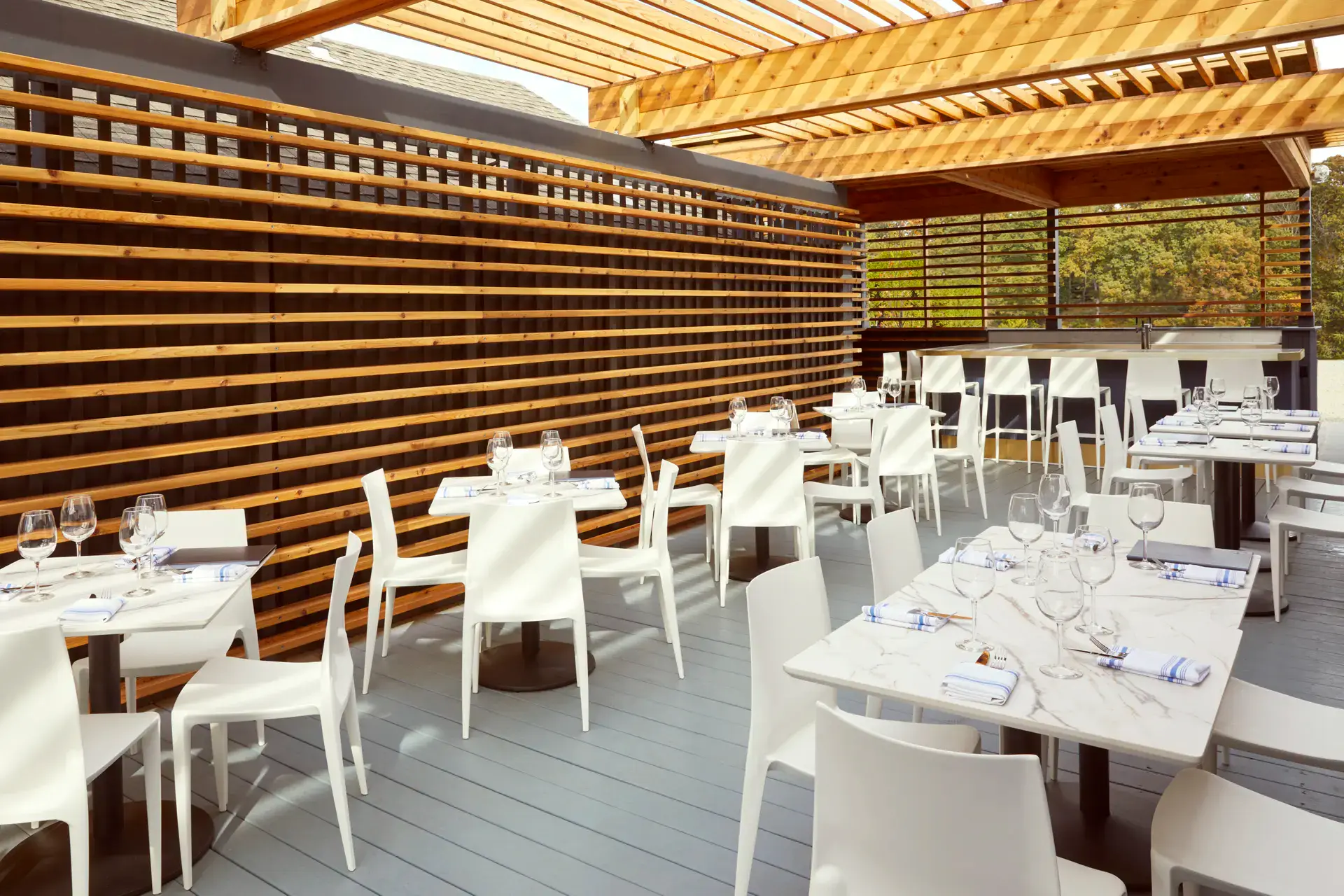 White chairs and marble-topped tables beneath a timber pergola on the restaurant terrace at The Bridge at Westport