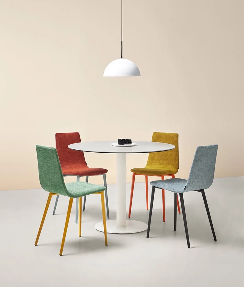 A round Sol pedestal table with green, red, yellow and blue chairs under a white pendant