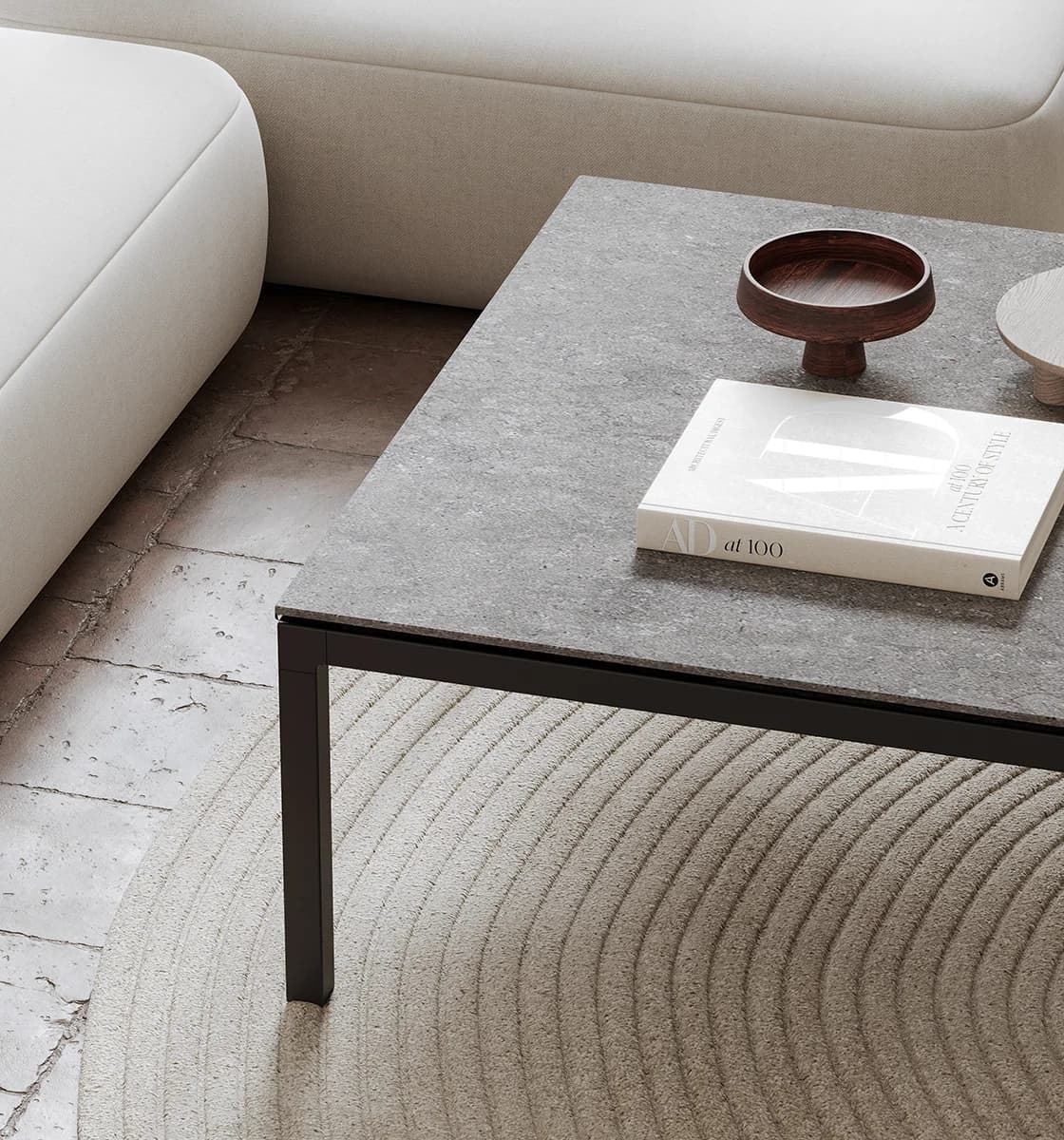 A grey porcelain table top on a slim black steel frame, beside a cream sofa on a stone floor