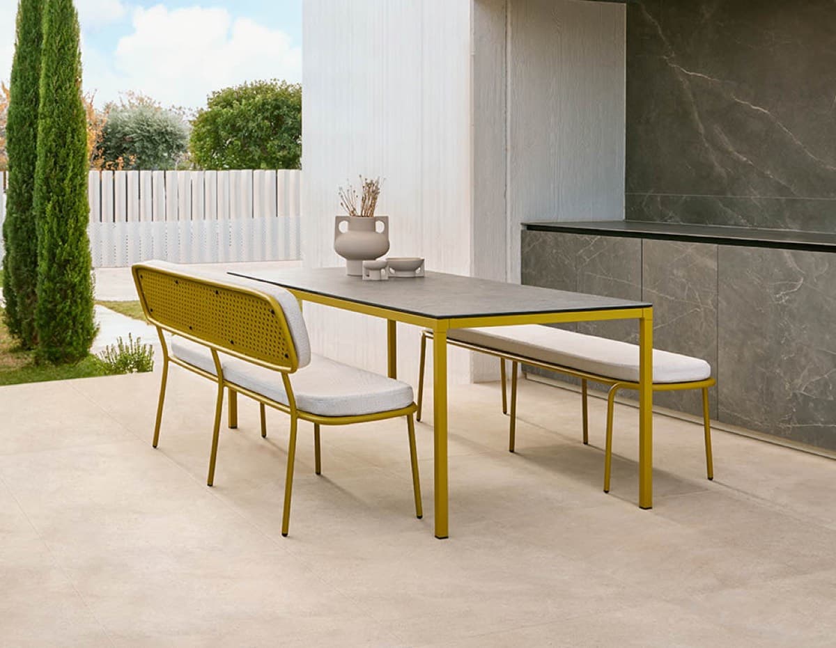 A yellow Abril dining table and matching seating beside pale stone walls
