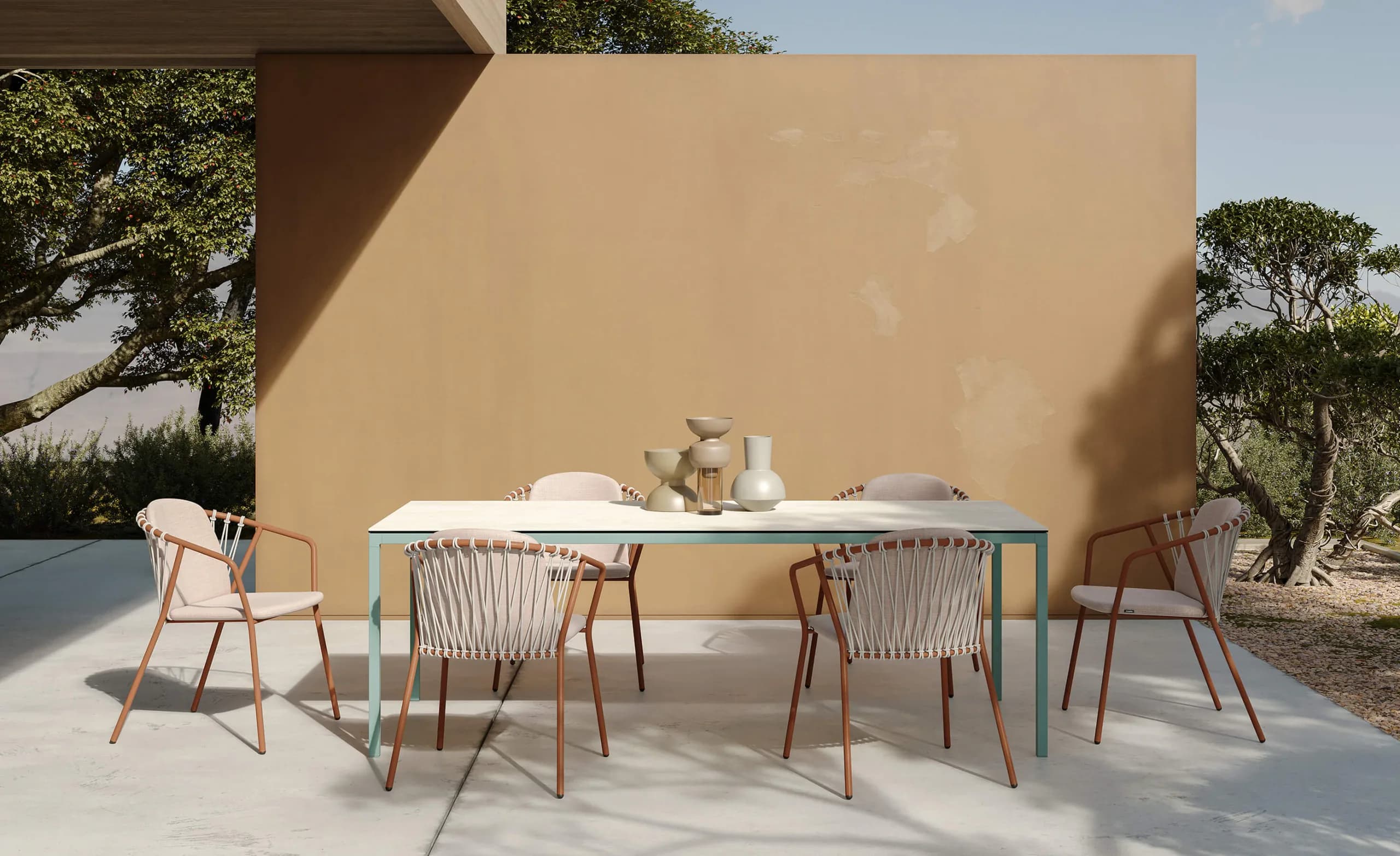 Musola Baga chairs around a Brise dining table on a terrace beside an ochre wall and olive trees