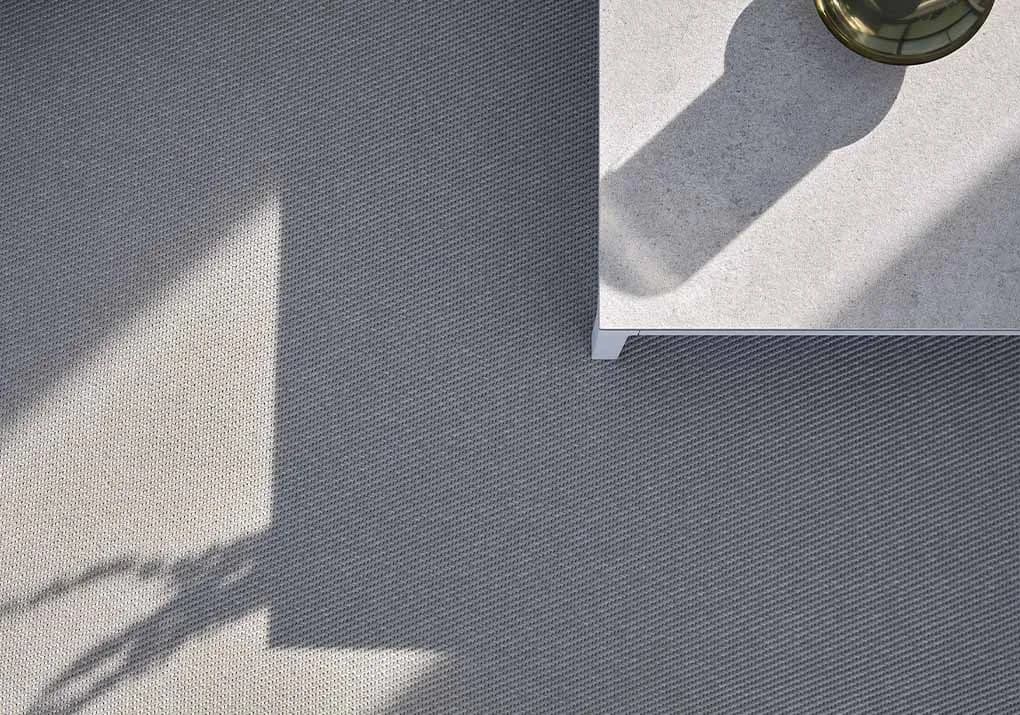 A grey Milpa outdoor rug on a concrete terrace in strong shadow
