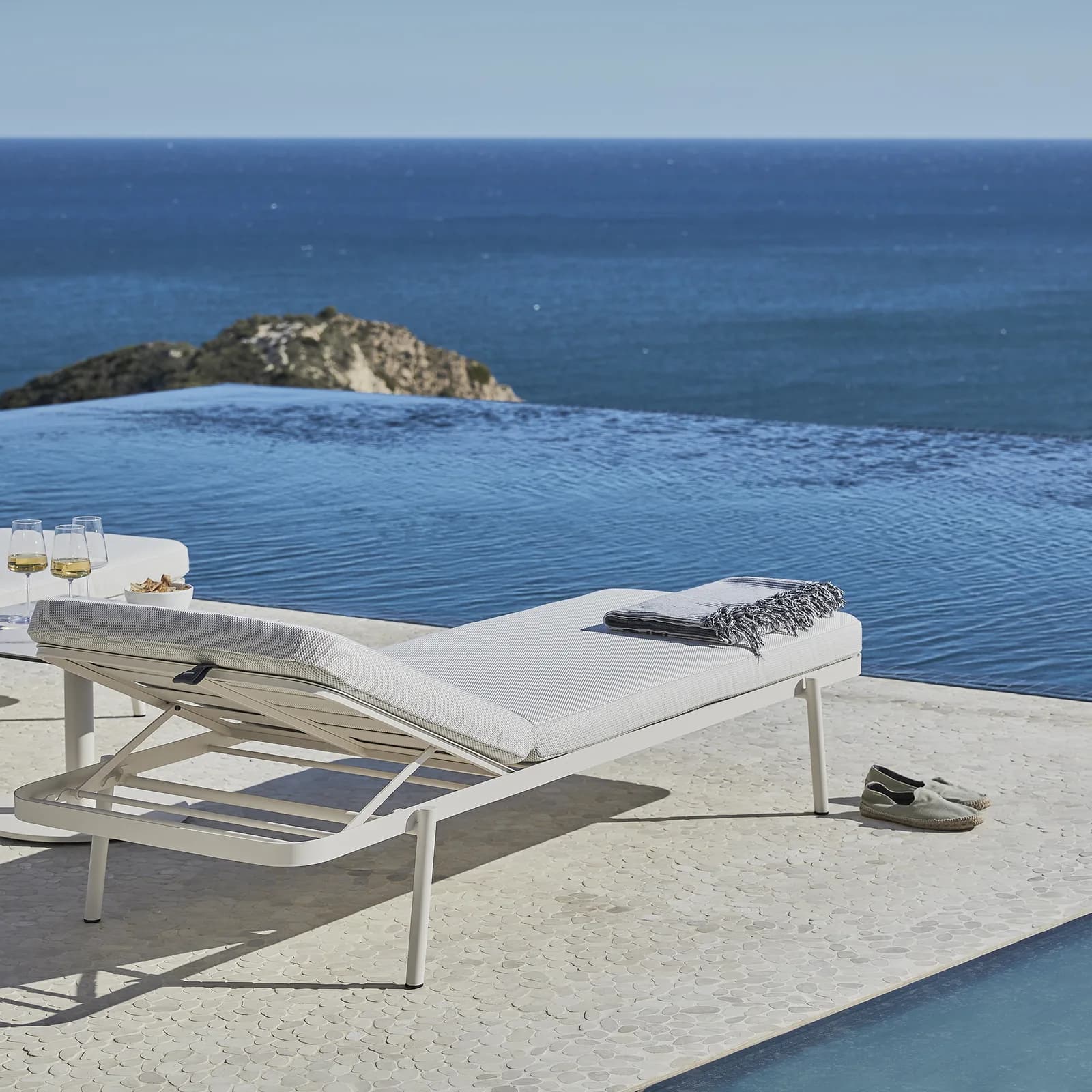 A white lounger on a terrace beside an infinity pool and the sea