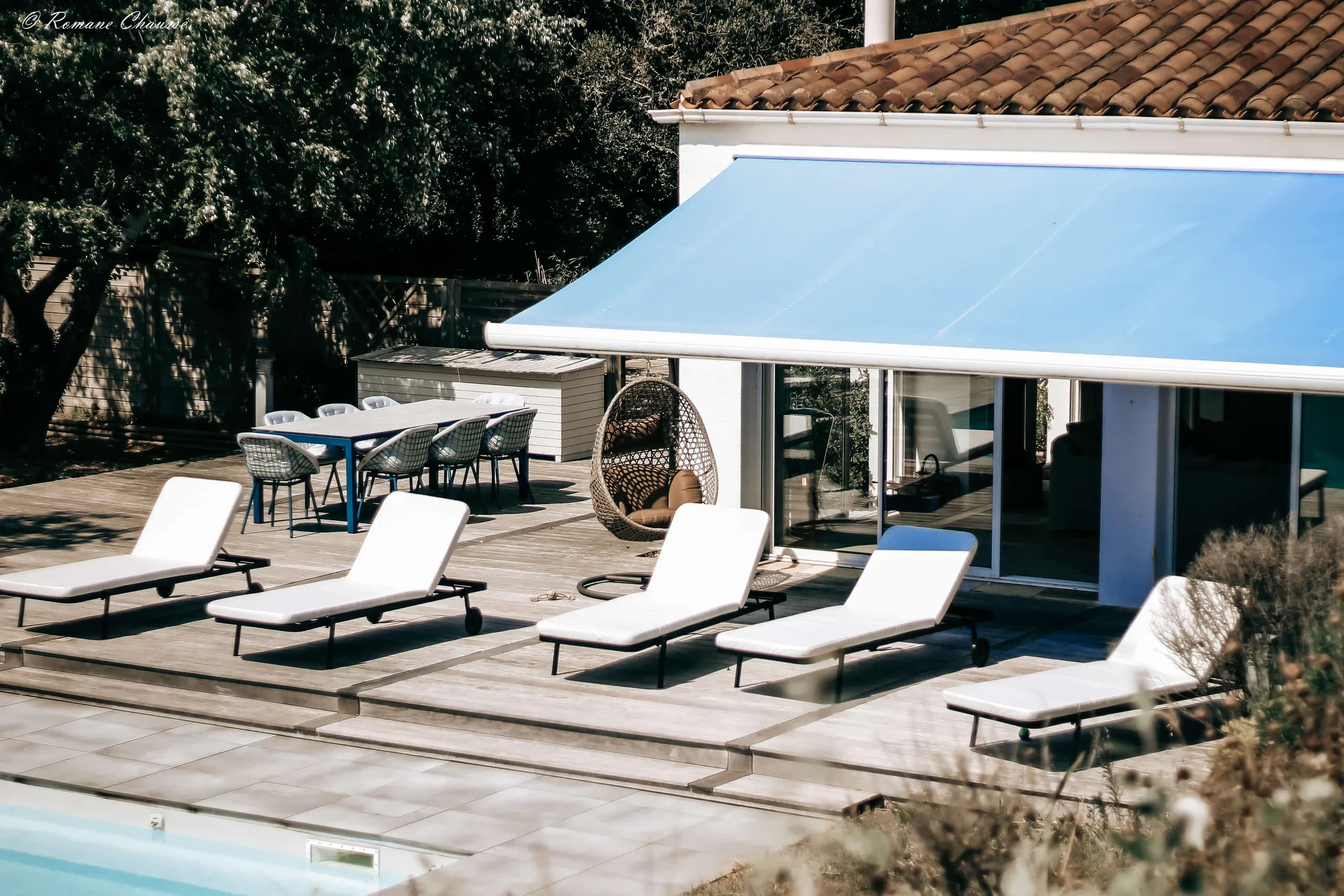 White loungers by a pool under a blue awning outside a house on Île d’Oléron
