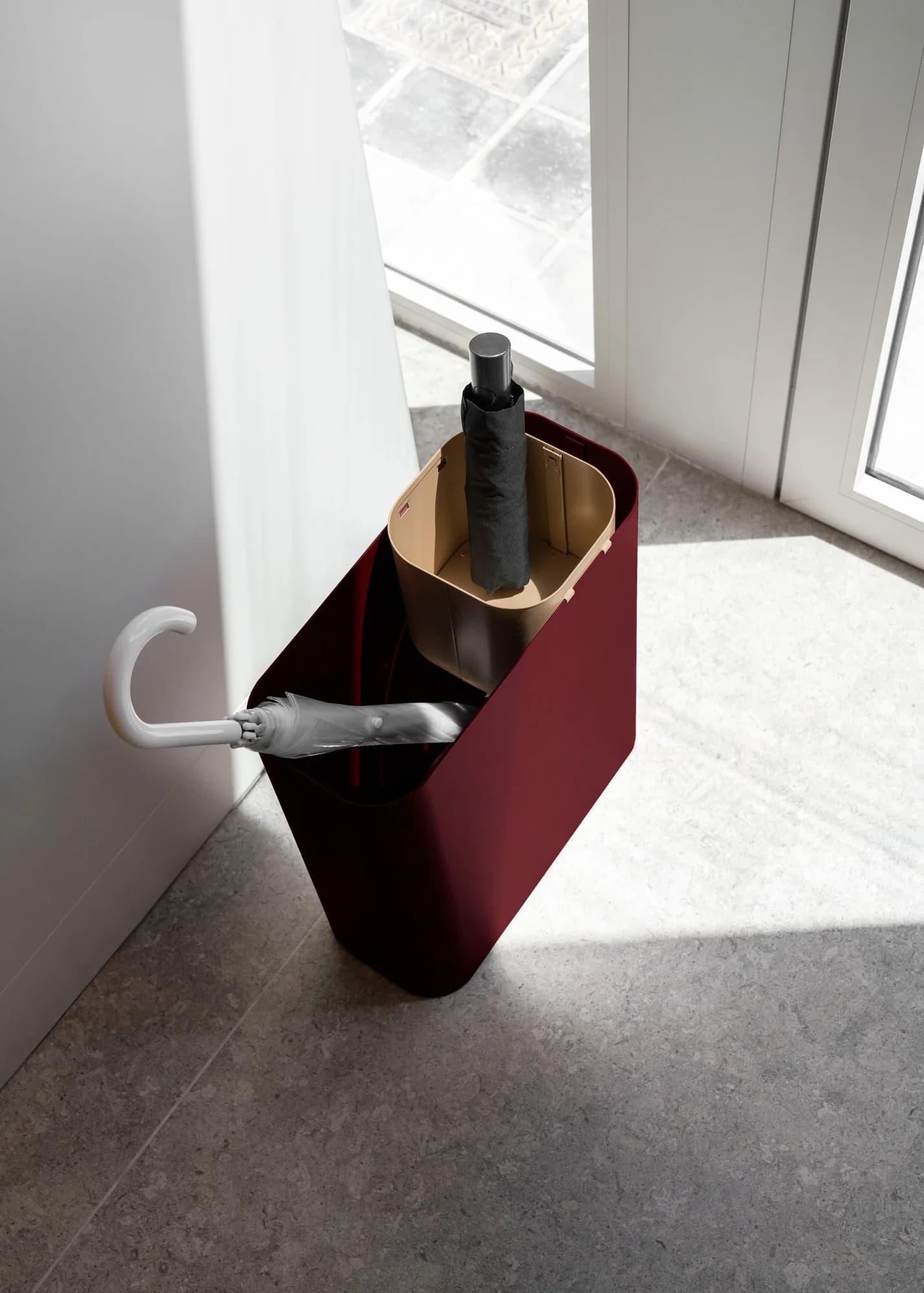 A burgundy umbrella stand by a window in a pale showroom